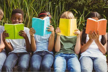 Children sitting on a wall reading books